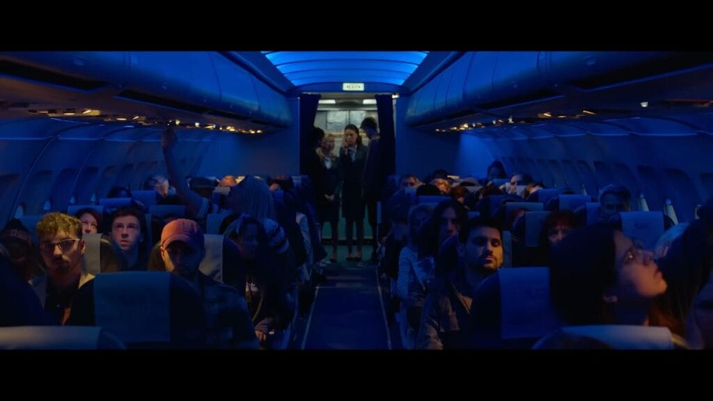 The interior cabin of a commercial airplane bathed in blue neon lighting with passengers seated in rows in Black Box.