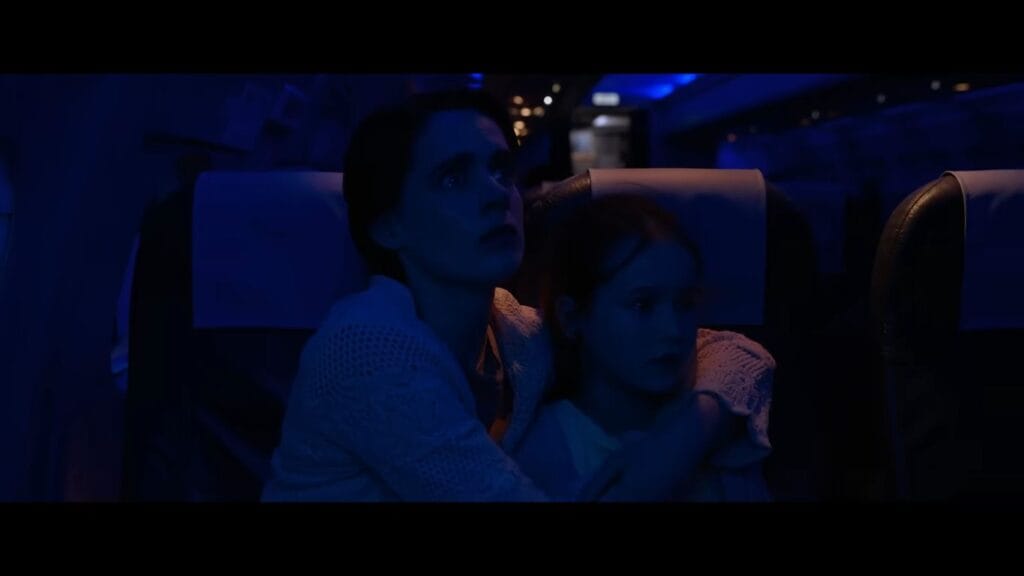 A frightened mother holding her young daughter tightly in an airplane seat under dark blue lighting in Black Box.