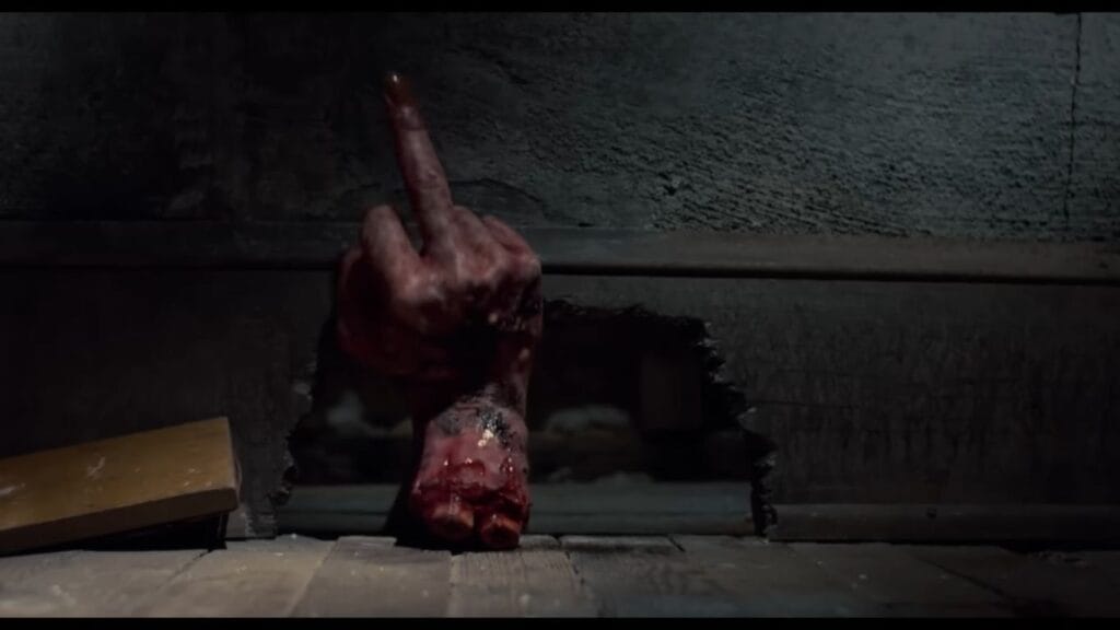 Ash's severed, blood-soaked possessed hand flipping the middle finger while emerging from a hole in the wall in Evil Dead II.