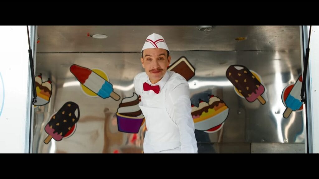 An ice cream man with a mustache, red bow tie, and white paper hat leaning out of his truck window with an unsettling smile in Ice Cream Man.