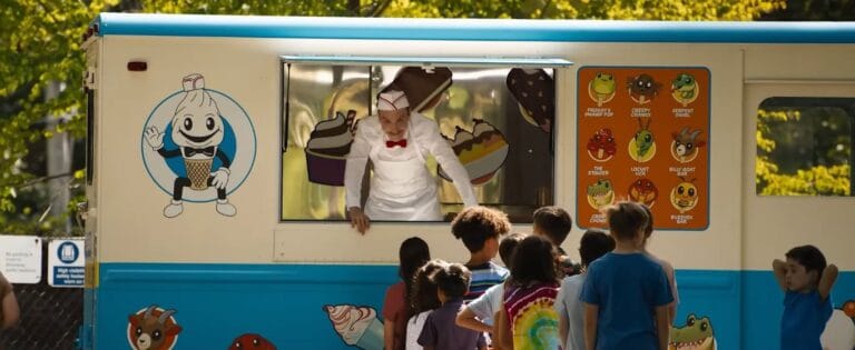 An ice cream man leaning out of his blue and white truck window to serve a group of eager children in Ice Cream Man.