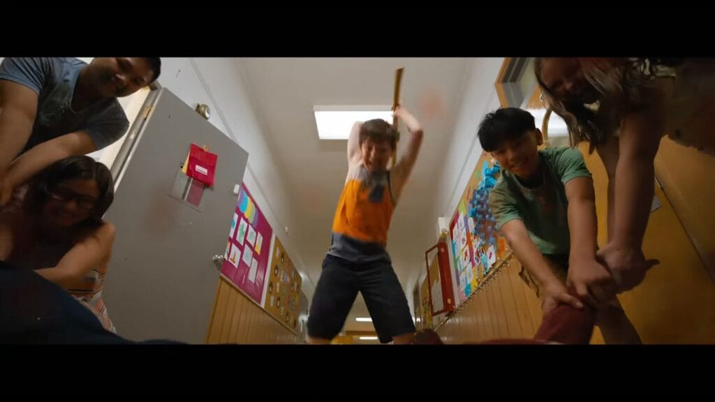A group of children aggressively swarming and attacking an adult in a brightly lit school hallway in Ice Cream Man.