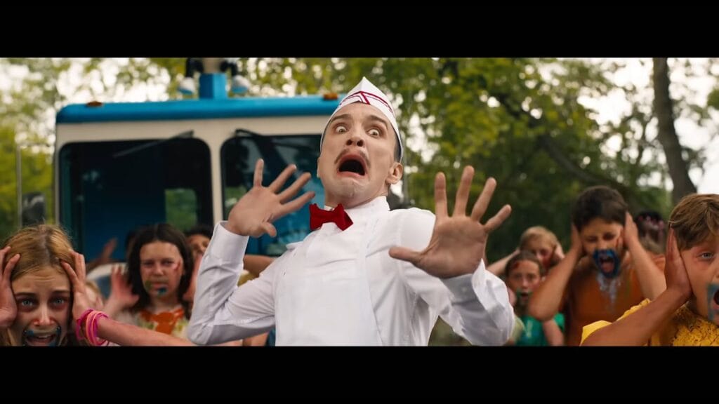 The ice cream man raising his hands in mock panic in front of his truck as children scream in the background in Ice Cream Man.