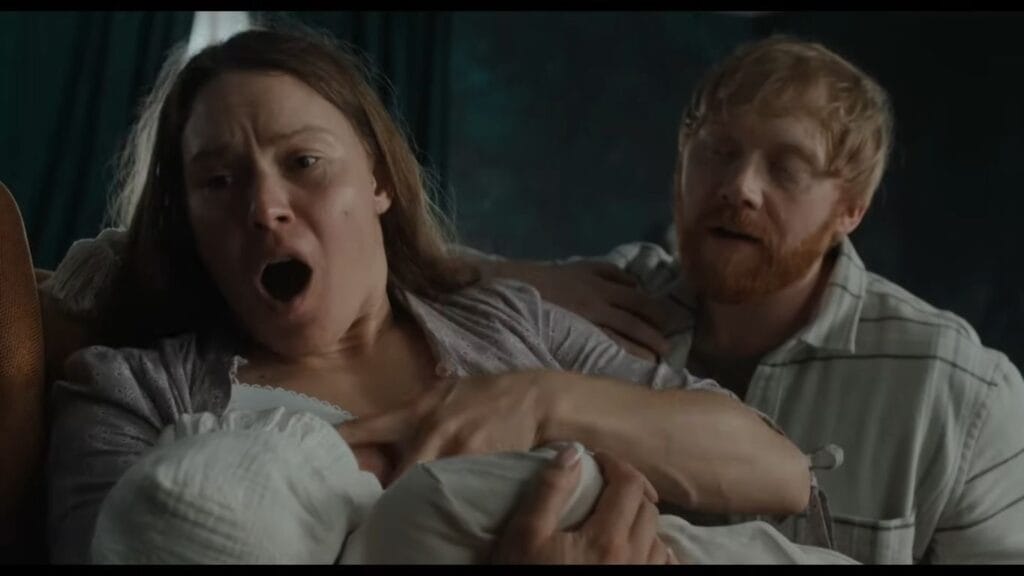 A woman screaming in pain and exhaustion while holding her newborn baby alongside a concerned man in Nightborn.
