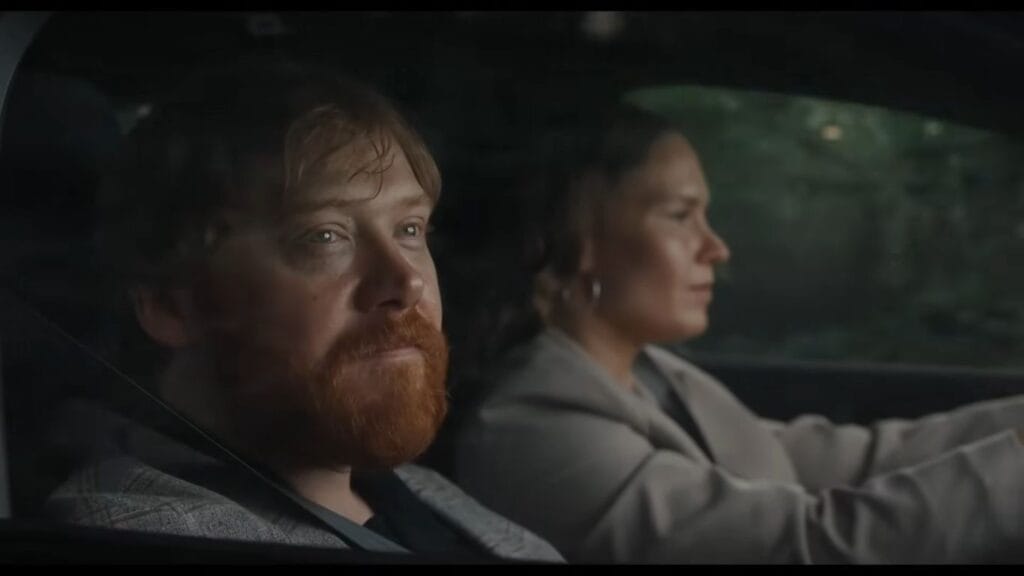 Rupert Grint as Jon with a red beard sitting in the passenger seat of a car looking out the window in Nightborn.