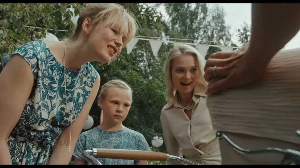 Three smiling family members leaning over outdoors to excitedly peer into a baby stroller in Nightborn.