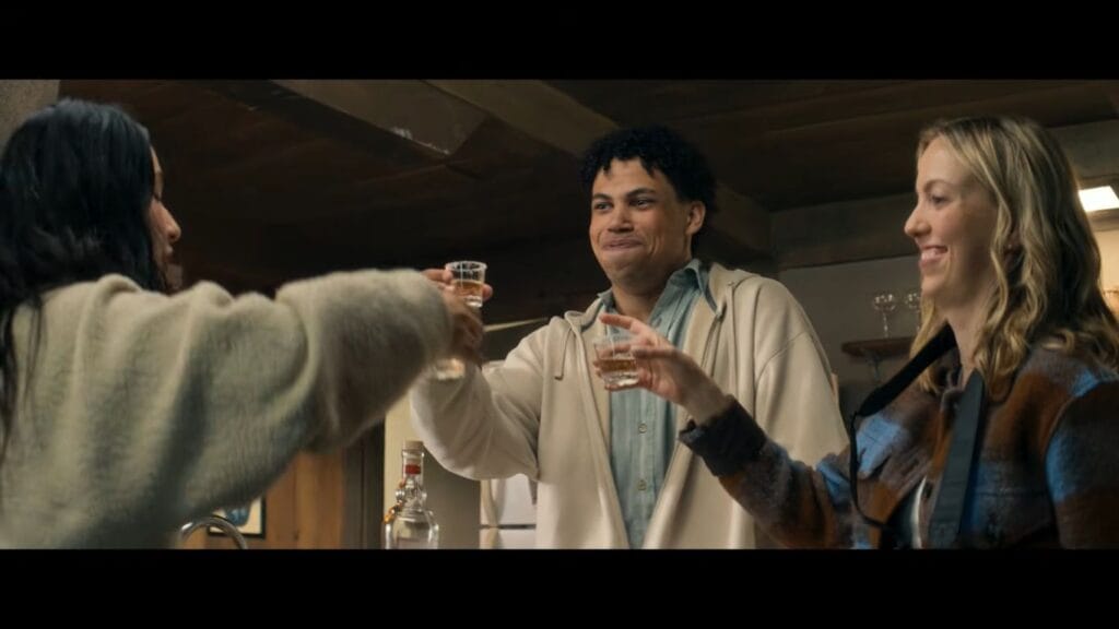Three young adults smiling and toasting shot glasses inside a wooden cabin in Sawtooth Mountain.