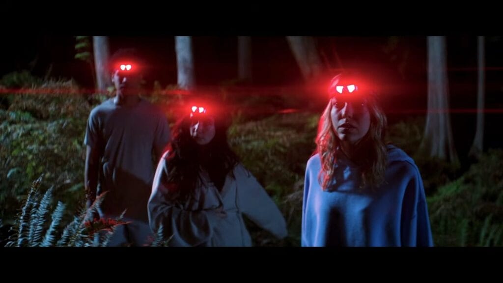 Three campers wearing bright red glowing headlamps walking through a dark forest at night in Sawtooth Mountain.