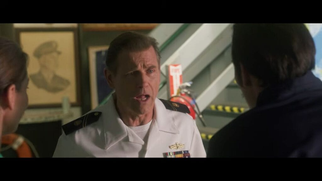 Michael Paré in a white naval captain uniform talking intently to crew members aboard a ship in Shark Terror.