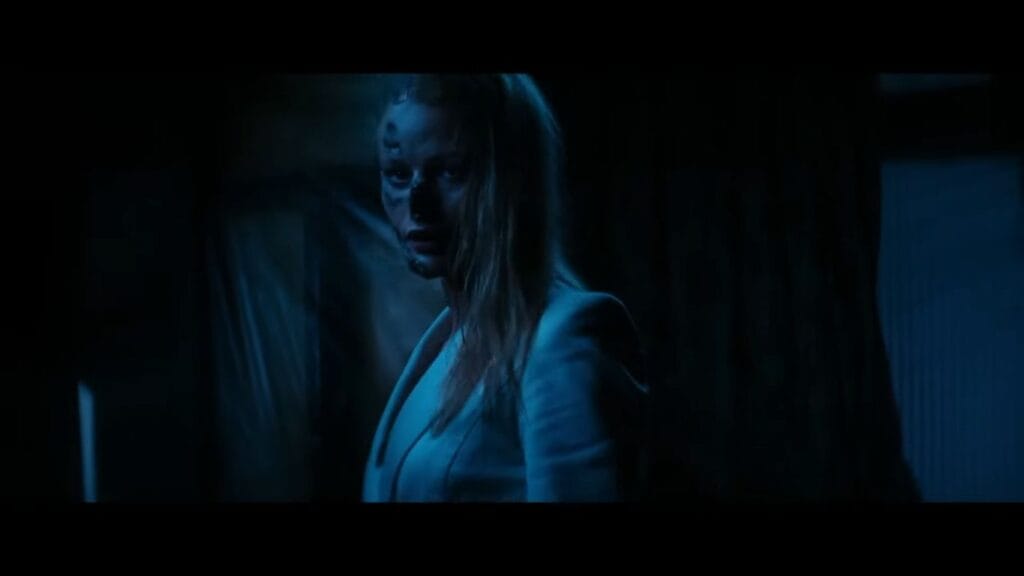 Damaged companion android Lily Sullivan standing in a blue-lit dark room with peeling facial skin in Soulm8te.