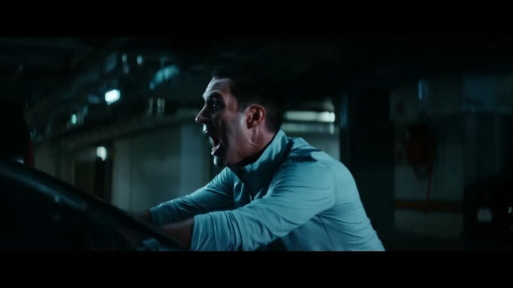 A man shouting in fear while leaning over a vehicle hood in a dark parking garage in Soulm8te.