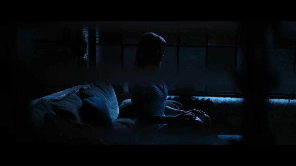 The dark silhouette of blonde android Sara sitting motionless on a sofa in a shadowy living room at night in Soulm8te.