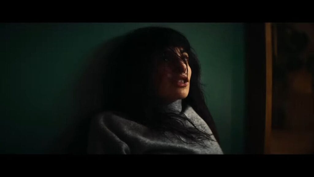 A woman in a grey turtleneck sweater looking up with a fearful and distressed expression in a dimly lit room in Soulm8te.
