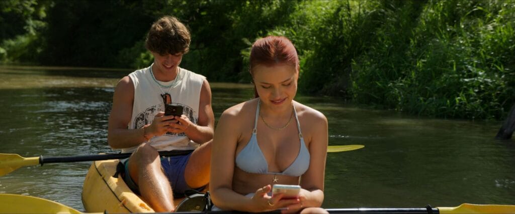 A young couple sitting in a yellow kayak looking down at their smartphones along a lush river in The Devil's Mouth.