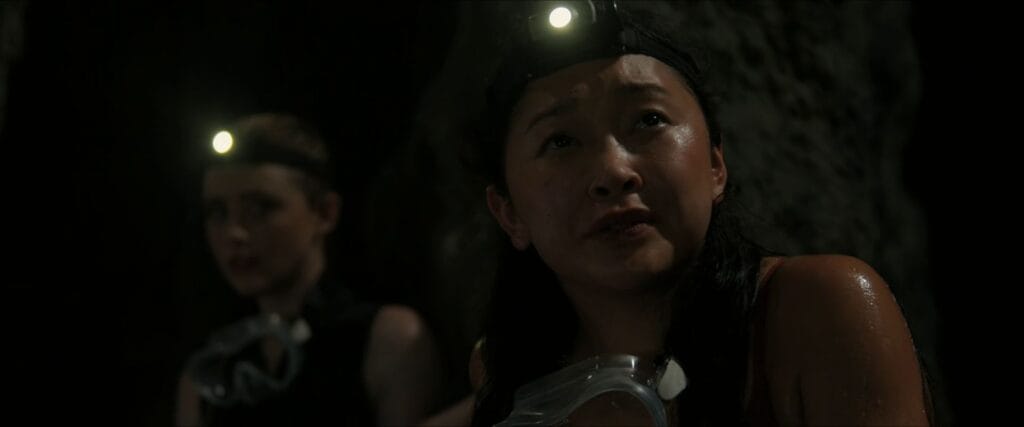 Lana Condor as Max wearing a headlamp looking up anxiously inside a dark flooded cave setting in The Devil's Mouth.