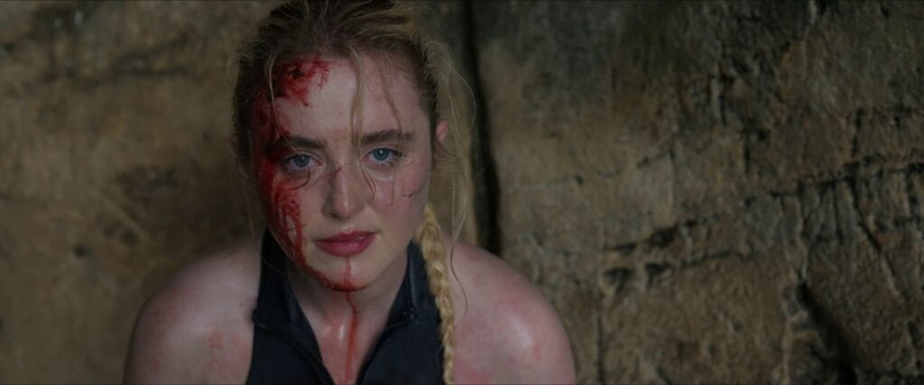 Close-up of Kathryn Newton as Sara with blood streaming down her face staring ahead inside a cave in The Devil's Mouth.