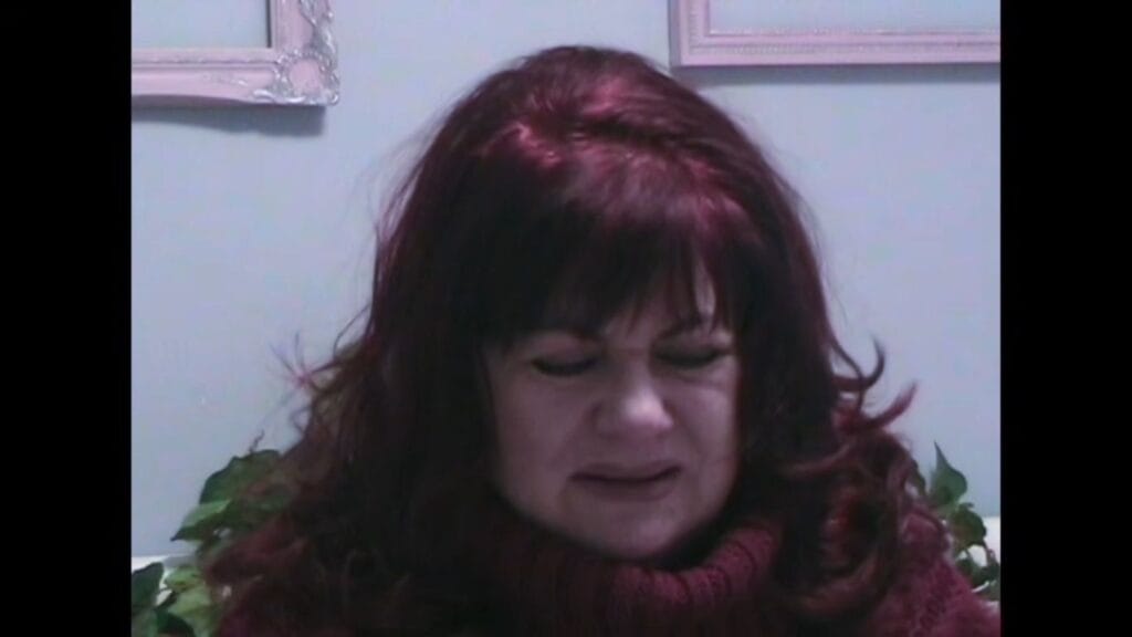 A woman with reddish-brown hair in a burgundy turtleneck looking down with an emotional, tearful expression in Tinsman Road.