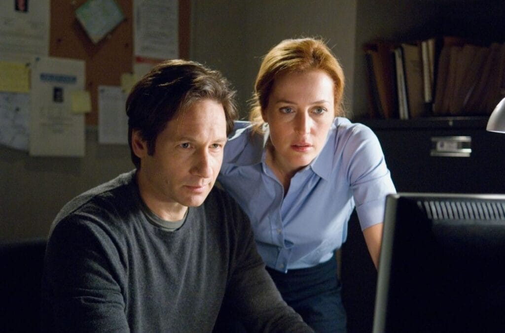 David Duchovny as Fox Mulder and Gillian Anderson as Dana Scully leaning over to look intently at a computer monitor in The X Files: I Want to Believe.