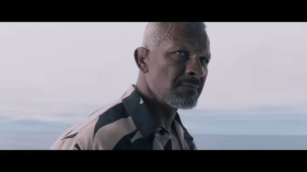 A rugged, short-haired man with scars on his face looking pensively off a boat deck in Above and Below.