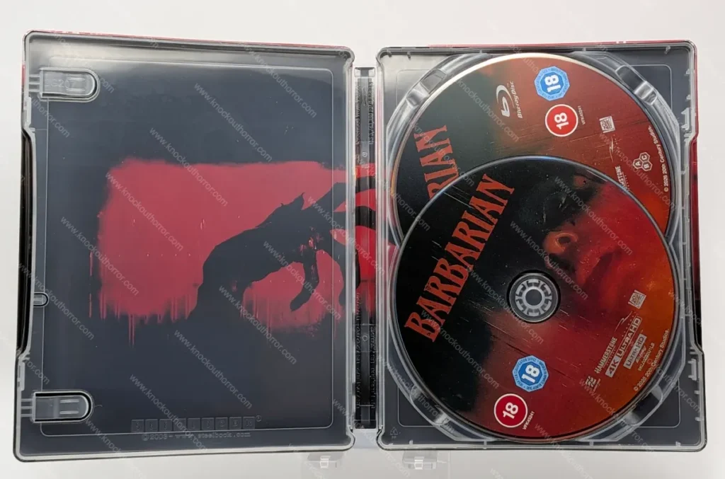Fully opened interior of the Barbarian steelbook with disc trays empty, revealing the continuous red and black silhouette artwork of a monstrous reaching hand.