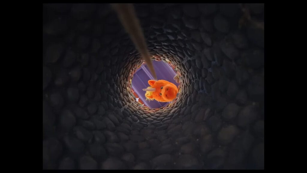 Point-of-view shot looking up from deep inside a stone well as Buddy the orange unicorn peers down over the ledge in Buddy.