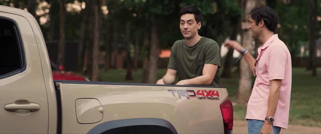 Two friends chatting casually by the back of a beige pickup truck parked outdoors in Deathwoods.