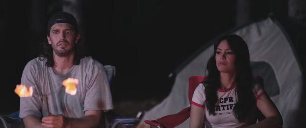 A man holding burning marshmallows on a stick next to an unimpressed woman sitting by a campfire in Deathwoods.