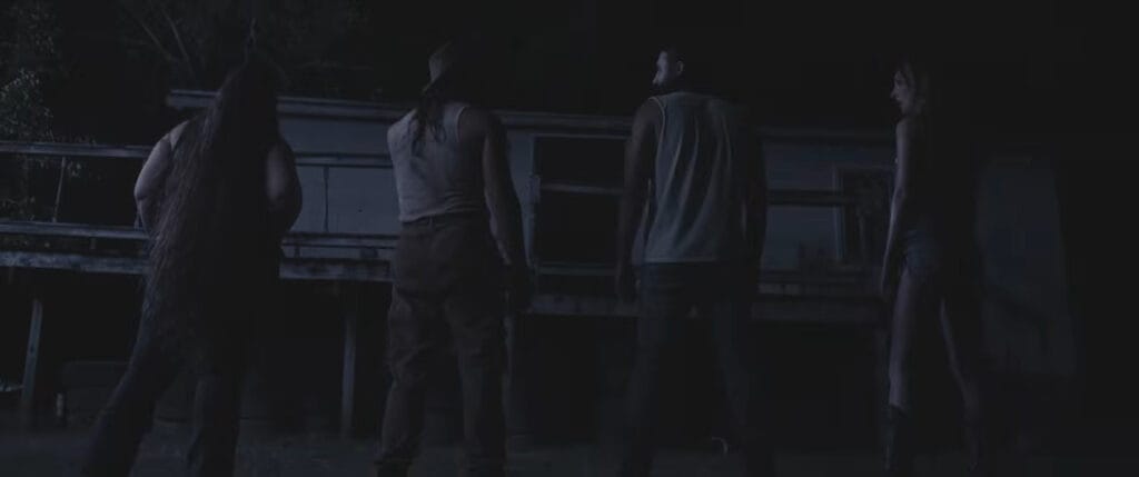 Four people standing with their backs to the camera looking toward a dark, dilapidated cabin at night in Deathwoods.