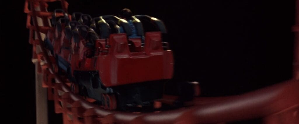 Close-up shot of the red Devil's Flight roller coaster cars speeding along the dark track in Final Destination 3.