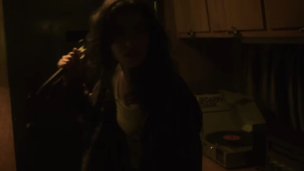 Dakota Gorman as Lena brandishing a metal weapon while moving cautiously through a dark camper trailer in Hellcat.