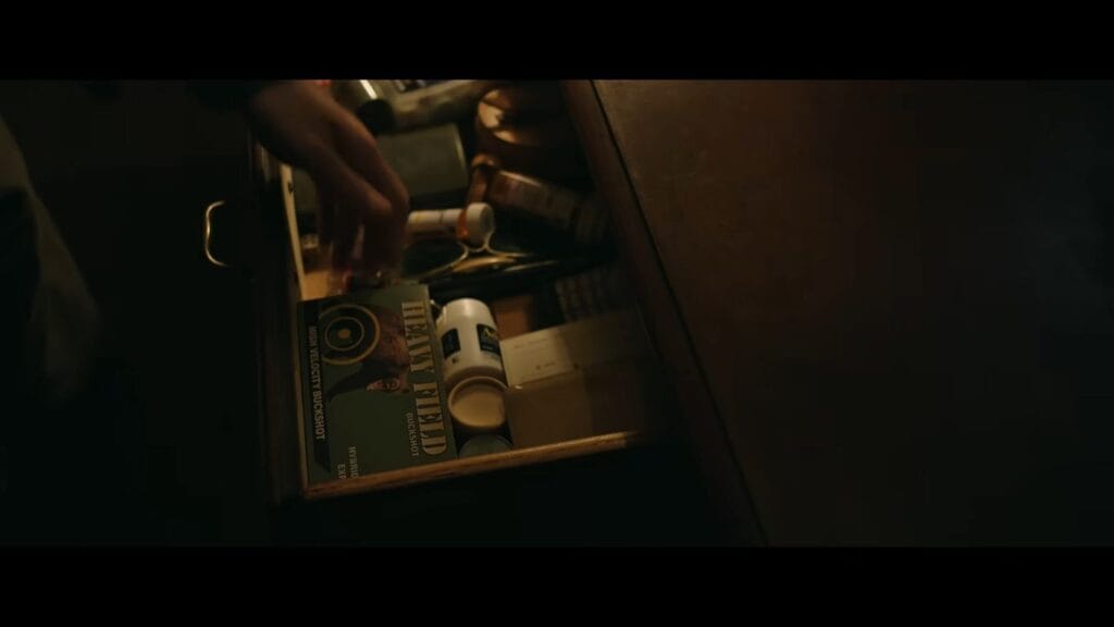 A character's hand reaching into a cluttered wooden drawer toward a green box of Heavy Field buckshot shotgun shells in Resident Evil.