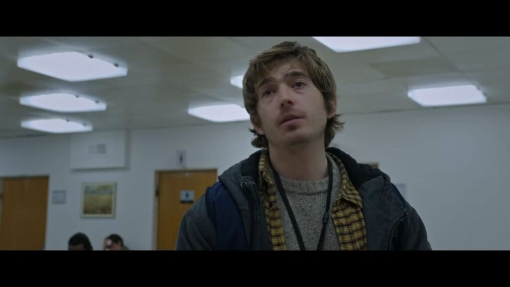 Austin Abrams as Bryan looking bewildered under harsh fluorescent lights inside a hospital corridor in Resident Evil.