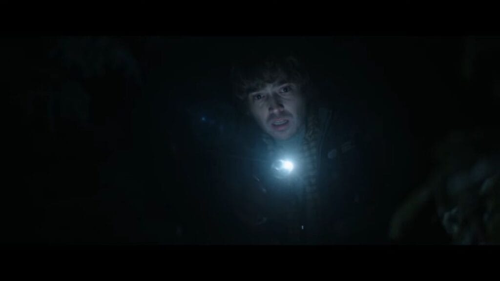 Bryan aiming a bright flashlight beam into pitch darkness with a terrified expression in Resident Evil.