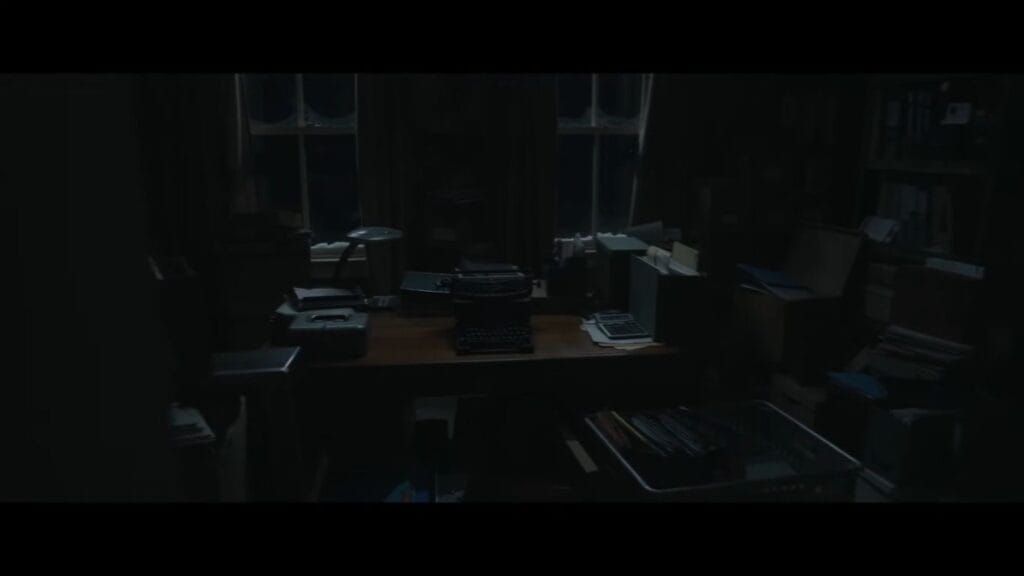 A dark, eerie office room featuring a vintage typewriter sitting on a cluttered wooden desk in Resident Evil.