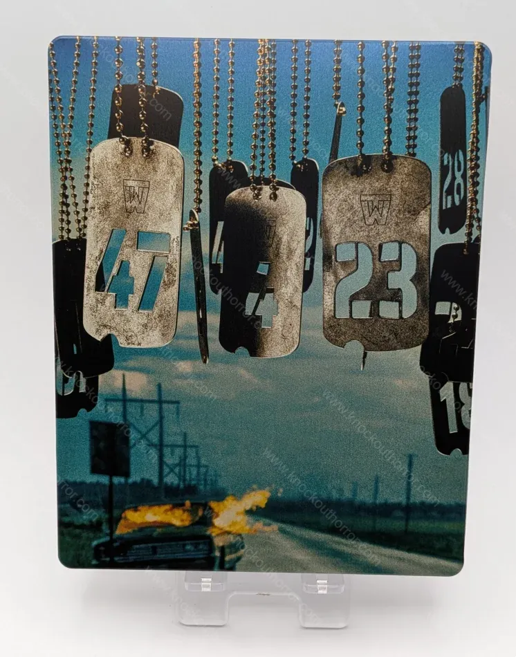 Rear cover of The Long Walk 4K steelbook featuring hanging military dog tags with walker numbers over a burning car on a deserted highway.