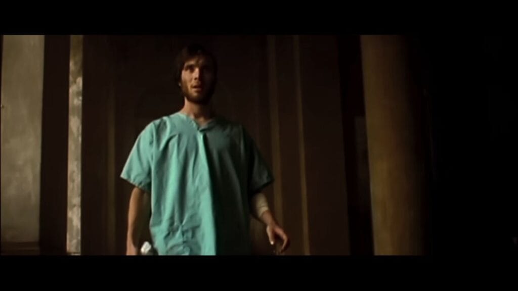Jim standing in hospital scrubs looking stunned and disoriented inside an empty hallway in 28 Days Later.