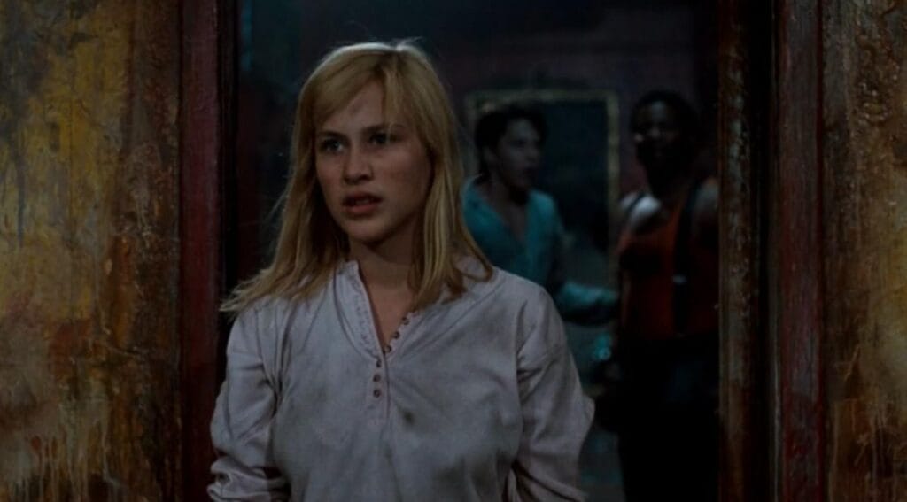 Patricia Arquette as Kristen standing alert in a hospital nightshirt in front of a weathered doorway in A Nightmare on Elm Street 3: Dream Warriors.