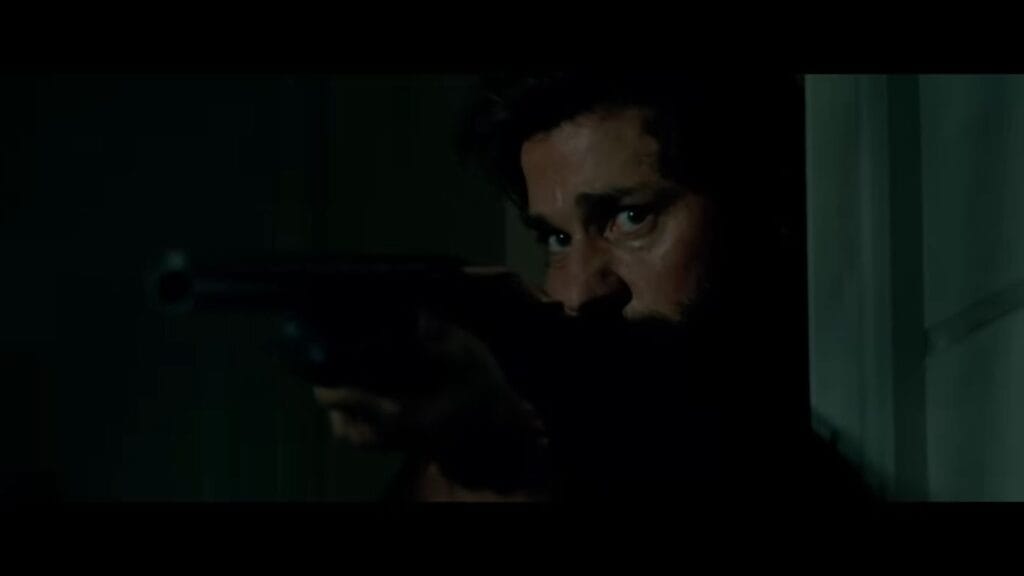 A tense close-up of Lee aiming a shotgun around a dark doorway in A Quiet Place.