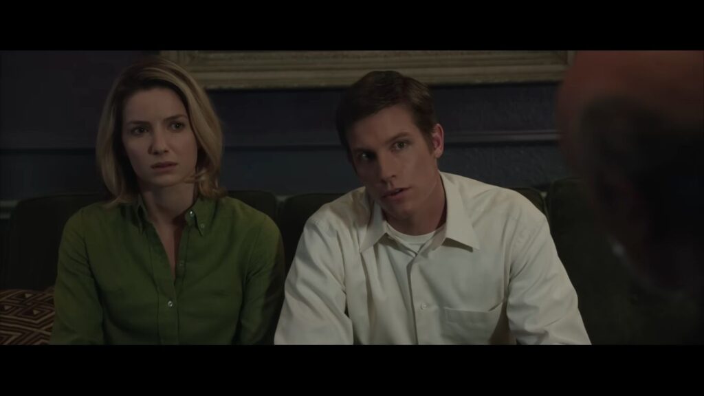 Mia and John looking concerned and listening during a serious conversation on the couch in Annabelle.