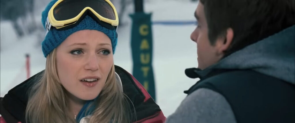 Emma Bell as Parker wearing a blue beanie and ski goggles talking to Dan on the ski slopes in Frozen.