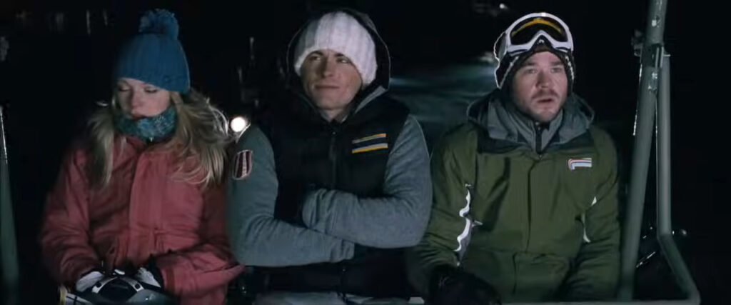 Parker, Dan, and Joe sitting side-by-side bundled up on a stopped ski chairlift in the dark in Frozen.