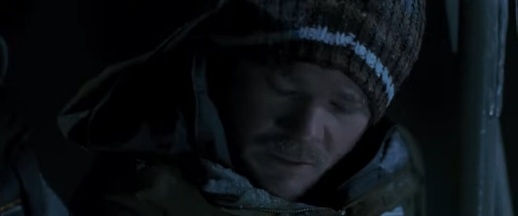 Shawn Ashmore as Joe wearing a knit beanie and looking down nervously in the dark in Frozen.