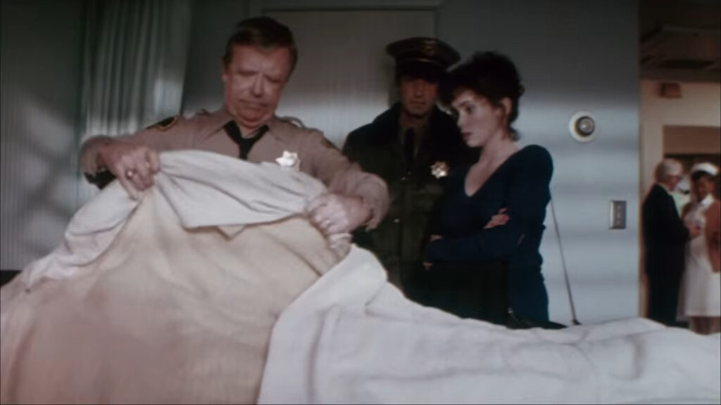 Stacey Nelkin as Ellie Grimbridge watching somberly as a police officer pulls back a morgue sheet in Halloween III: Season of the Witch.