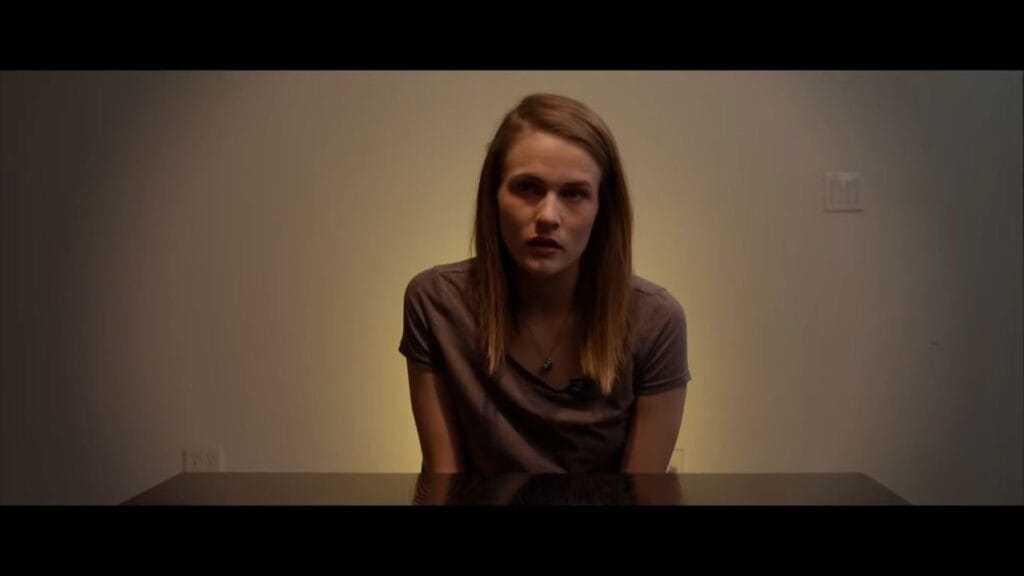 A woman being interviewed against a plain wall for a documentary segment in Hell House LLC.