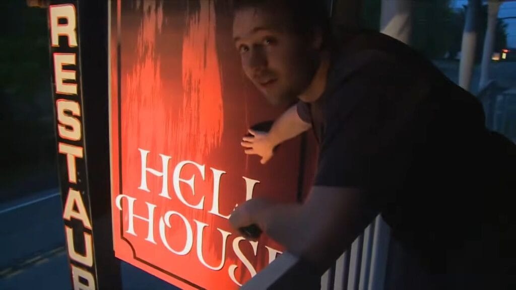 A crew member hanging a red sign reading Hell House on the front porch in Hell House LLC.