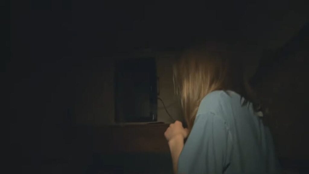 A woman looking anxiously in the dark toward a shadow in Hell House LLC.