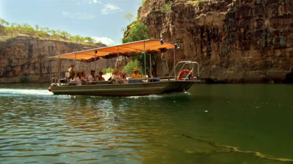 A river tour boat carrying passengers cruising along a river flanked by high rocky canyon walls in Rogue.