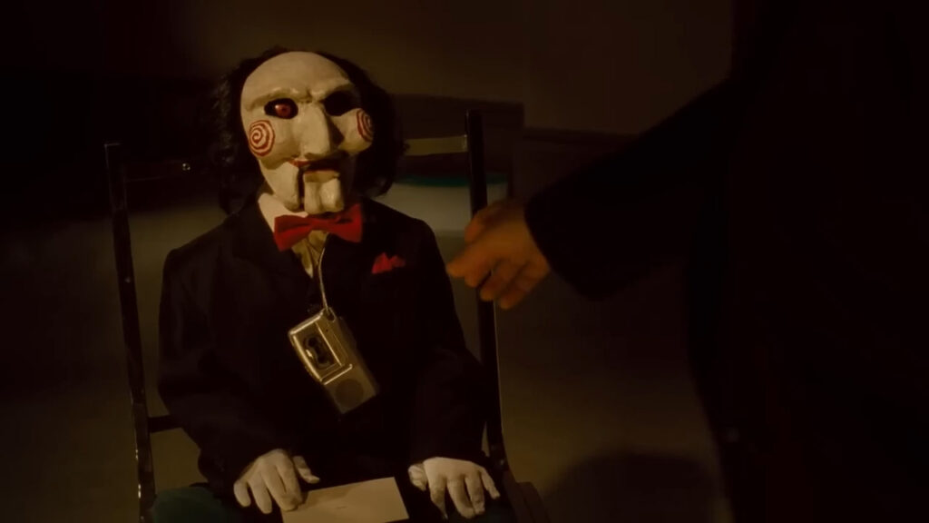 Billy the Puppet sitting on a chair with a cassette recorder in Saw IV.