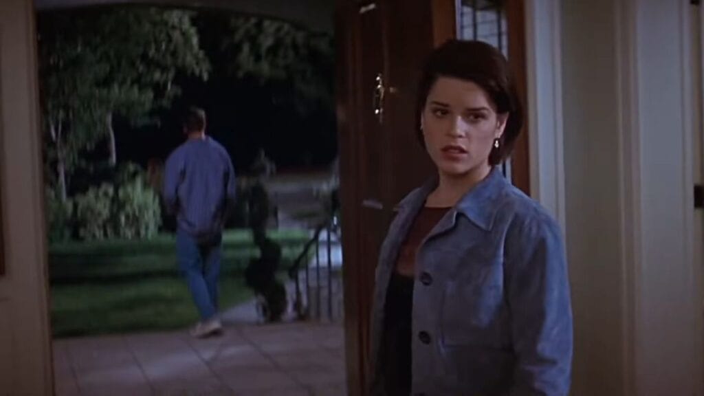 Neve Campbell as Sidney Prescott looking cautiously back over her shoulder in an open doorway in Scream 2.