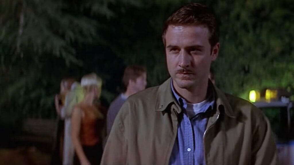 David Arquette as Dewey Riley looking serious and watchful while standing outside at night in Scream 2.